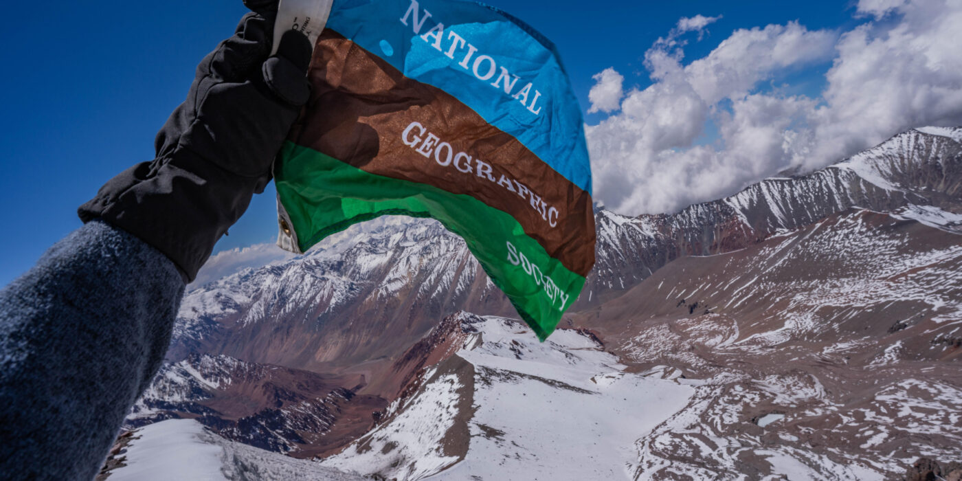 A National Geographic photographer holds the National Geographic Society flag at a mountain camp in Chile.